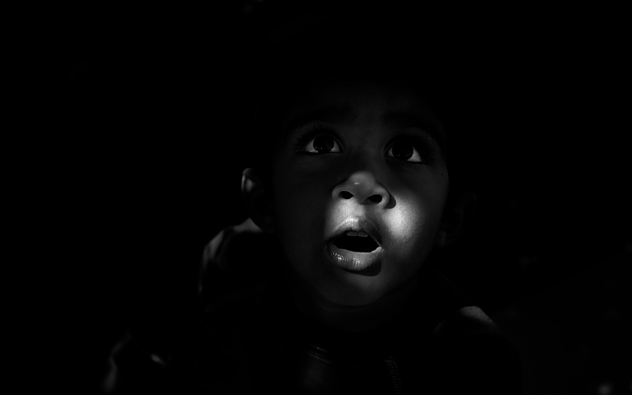 Черный удивление. Ребенок на черном фоне. Негр на темном фоне. Негр в темноте.